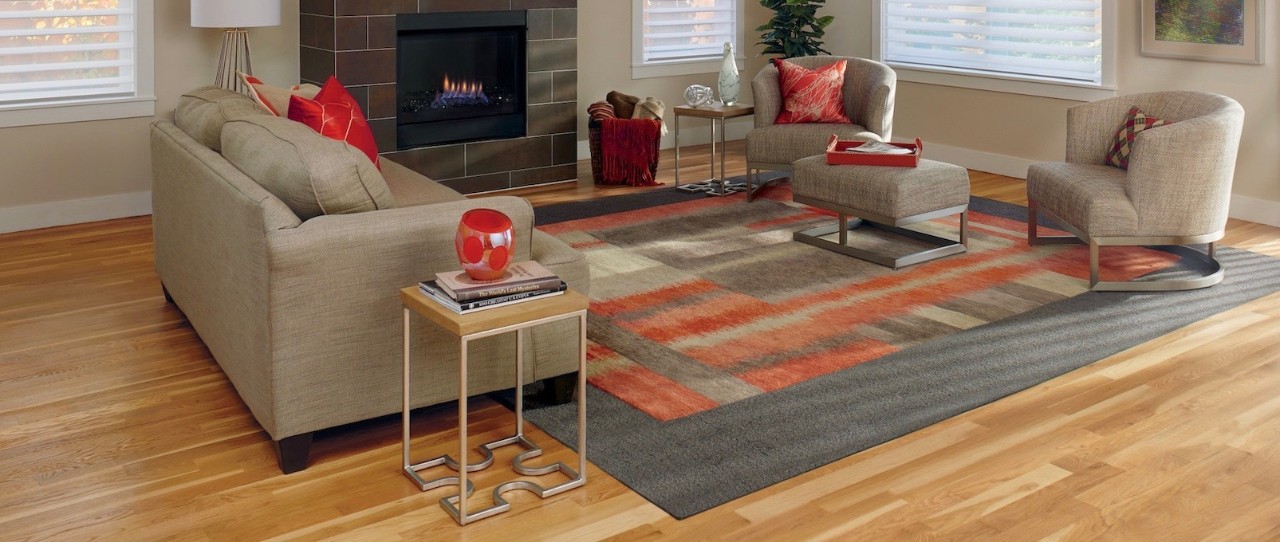 Modern living room with tan sofa and chairs. Fireplace and large pattern rug.